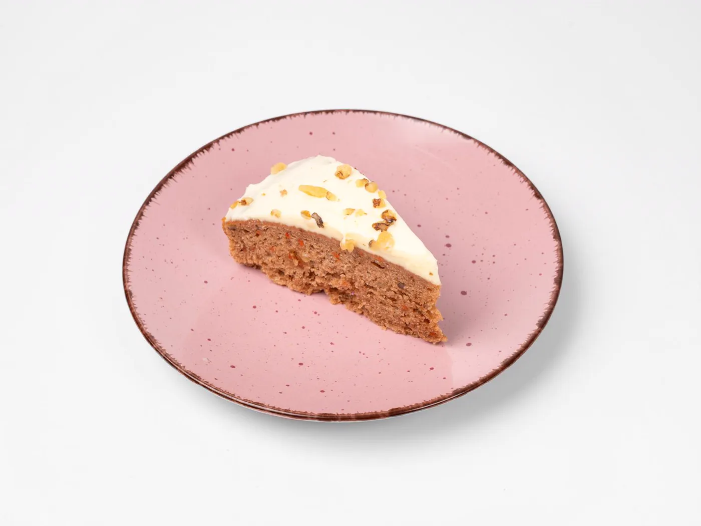 Ein Stück Karottenkuchen mit hellem Topping und Walnüssen auf einem rosa Teller